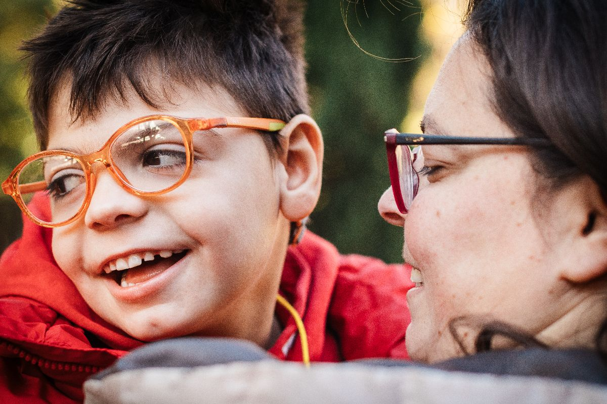 Mum holding son with complex disability wearing orange glasses and smiling happily 